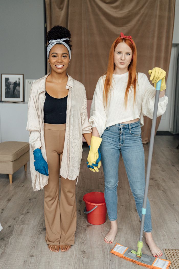 services-04 Two women smiling and holding hands while cleaning indoors, symbolizing teamwork.